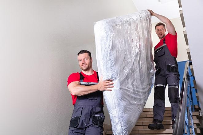 workers maneuvering a box spring through a narrow hallway in Perry